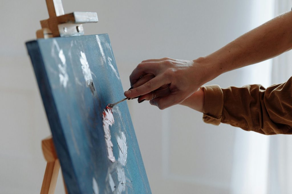 pexels photo 6732520 6732520 Close-up of a person painting with a spatula on a blue canvas indoors.